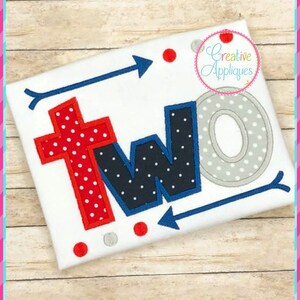 May include: Embroidered design of the word "two" in red, blue, and gray with white polka dots. The letters are outlined in blue and the design includes two arrows and red and gray polka dots.