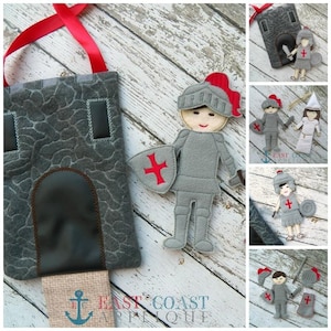 May include: A felt castle play set featuring a knight and a princess. The castle is grey with a brown door and a red cross on the shield. The knight is wearing grey armour and a red helmet. The princess is wearing a white dress and a white crown.