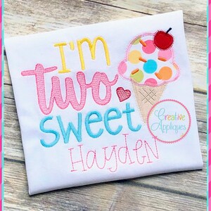May include: A white onesie with pink, blue, and yellow embroidery that says "I'm two sweet Hayden". The onesie also features an embroidered ice cream cone with a cherry on top.