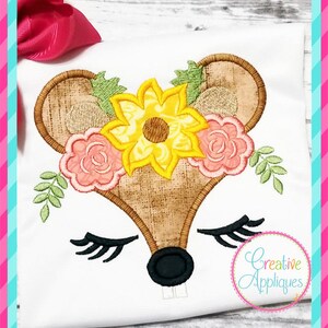 May include: Embroidered applique design of a mouse face with closed eyes, a black nose, and a sunflower and pink roses on its head. The design is on a white fabric background.