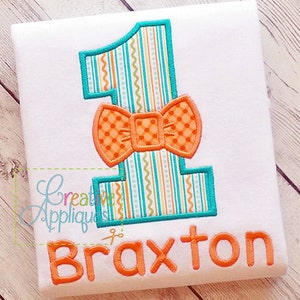 May include: A white onesie with an orange bow tie and a turquoise and orange number one. The onesie has the name "Braxton" embroidered on the bottom.