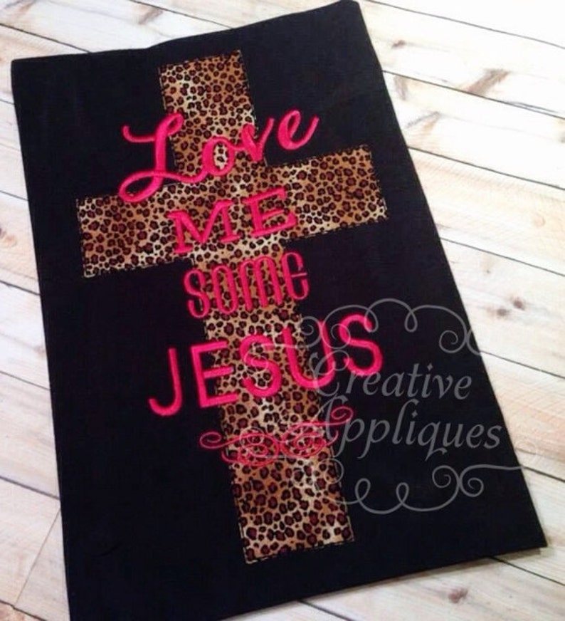 May include: Black fabric with a leopard print cross and the words "Love Me Some Jesus" embroidered in pink.
