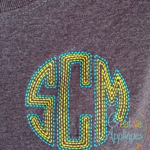 May include: Dark gray t-shirt with a stitched monogram in a circle. The monogram features the letters SCM in a gradient of yellow, green, and blue. The design is embroidered with a textured stitch.