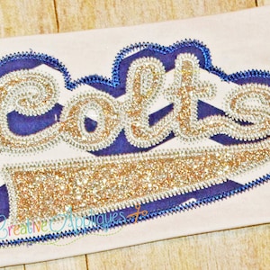May include: A gold glitter iron-on patch with the word "Colts" in a blue and white striped background. The patch is outlined in blue.