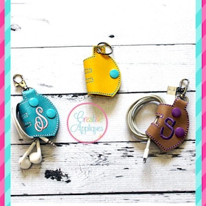 May include: Three leather cord organizers with snap closures and embroidered initials. The organizers are in teal, yellow, and brown with contrasting colored buttons.