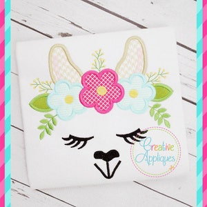 May include: Embroidered design of a llama face with closed eyes, a black nose, and a flower crown. The crown features pink, blue, and white flowers with green leaves.