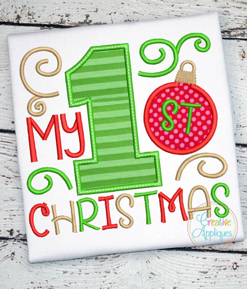 May include: A white onesie with the text "My 1st Christmas" in red and gold embroidery. The number 1 is green and striped. A red and white ornament with the letters "1st" is above the number 1.