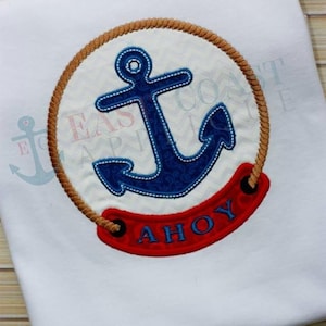 May include: White t-shirt with a nautical design. A blue anchor with a white outline is centered within a circular frame of rope. The word "AH0Y" is displayed in red below the anchor. The text "East Coast Apparel" is visible.