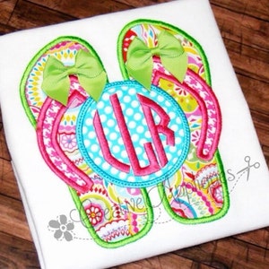 May include: A pair of colorful flip-flop shaped appliques with a green outline and a pink and blue monogram in the center. The monogram is surrounded by a turquoise circle with white polka dots.
