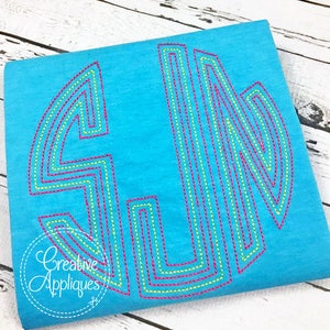 May include: A turquoise t-shirt with a large, multi-colored monogram letter "L" embroidered on the front. The letter is outlined in pink, yellow, and green thread.
