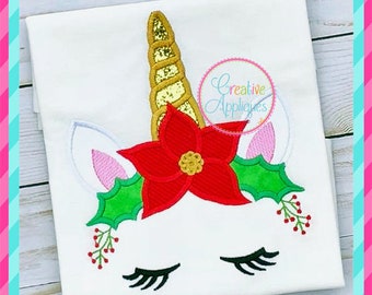 May include: Embroidered design of a unicorn with a red poinsettia flower, green holly leaves, and a gold horn. The unicorn has closed eyes and pink ears.