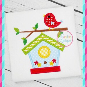 May include: A red bird with white polka dots sits on a branch above a blue and green birdhouse with a yellow and white checkered window. The birdhouse has a red base and white flowers on the front. The image includes the text "Creative Appliques".