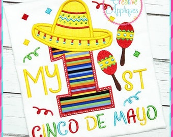 May include: A white t-shirt with an embroidered design featuring a colorful striped number one wearing a yellow sombrero, maracas, and the text "My 1st Cinco de Mayo".