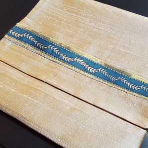 May include: A gold fabric pouch with a teal ribbon trim featuring a gold leaf design.
