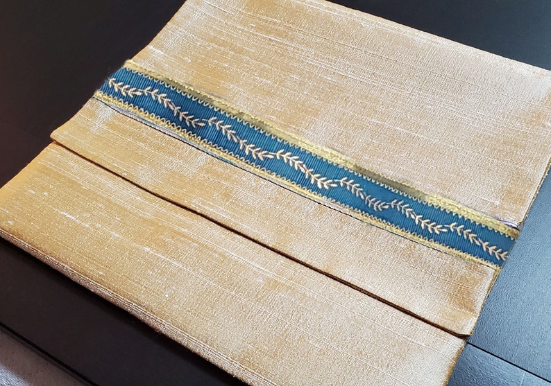 May include: A gold fabric pouch with a teal ribbon trim featuring a gold leaf design.