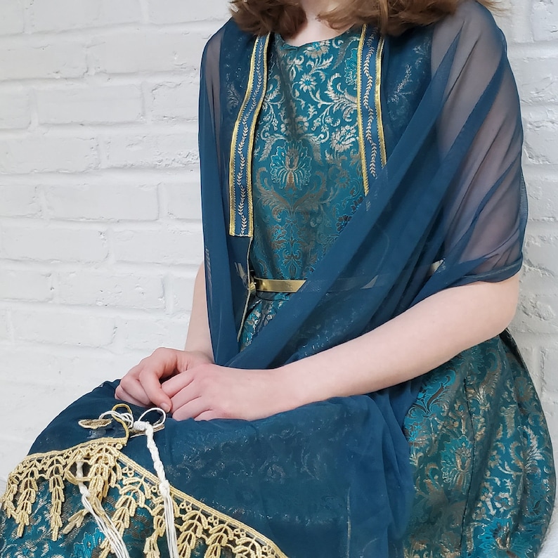 May include: A teal blue dress with a gold belt and a matching teal blue sheer shawl. The dress has a floral pattern and gold trim.
