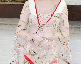 May include: A white sheer shawl with red trim and floral embroidery. The shawl is made of a delicate fabric and has a flowing design.