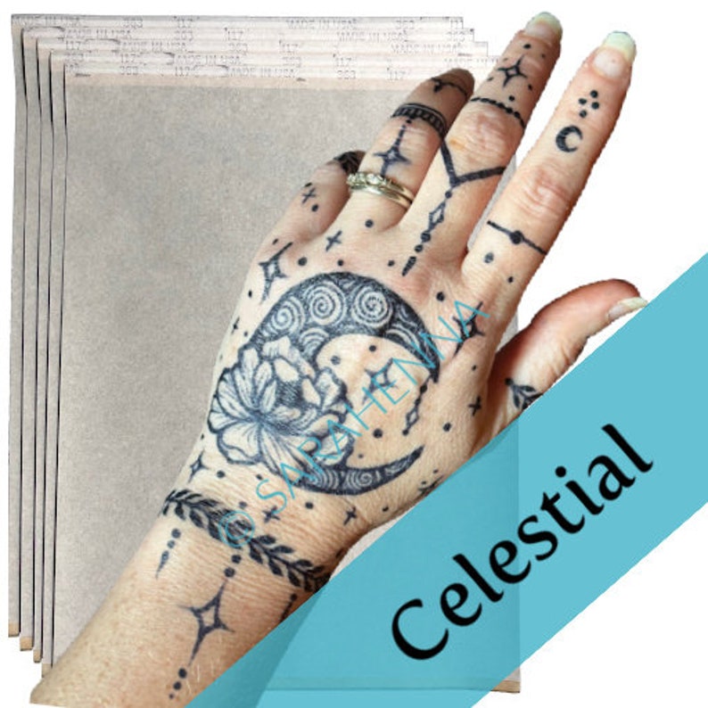 Puede incluir: Un paquete de 6 hojas de papel de transferencia para crear tatuajes temporales. El papel es marr&oacute;n claro y tiene una textura lisa. La imagen muestra una mano con un tatuaje temporal de una luna creciente, estrellas y una flor.