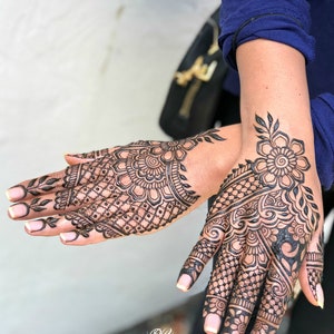 May include: Close-up of two hands with intricate black henna designs. The designs feature floral patterns, geometric shapes, and delicate lines.