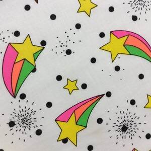 May include: White fabric with a repeating pattern of black dots, green, pink, and orange shooting stars with yellow stars in the center.