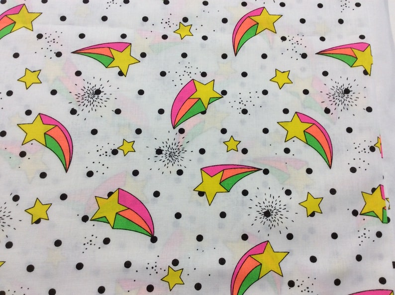 May include: White fabric with a repeating pattern of black polka dots, green, pink, and orange shooting stars with yellow stars in the center.