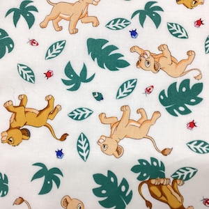May include: White fabric with a repeating pattern of cartoon lion cubs in various poses. The design includes green leaves, red ladybugs, and blue insects. The fabric is suitable for children's crafts and apparel.