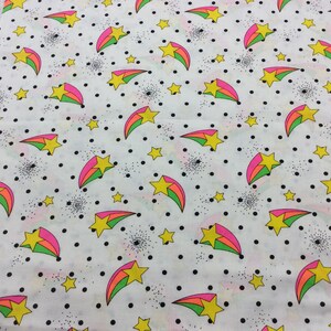 May include: White fabric with a repeating pattern of yellow stars and pink, green, and blue shooting stars on a white background with black polka dots.