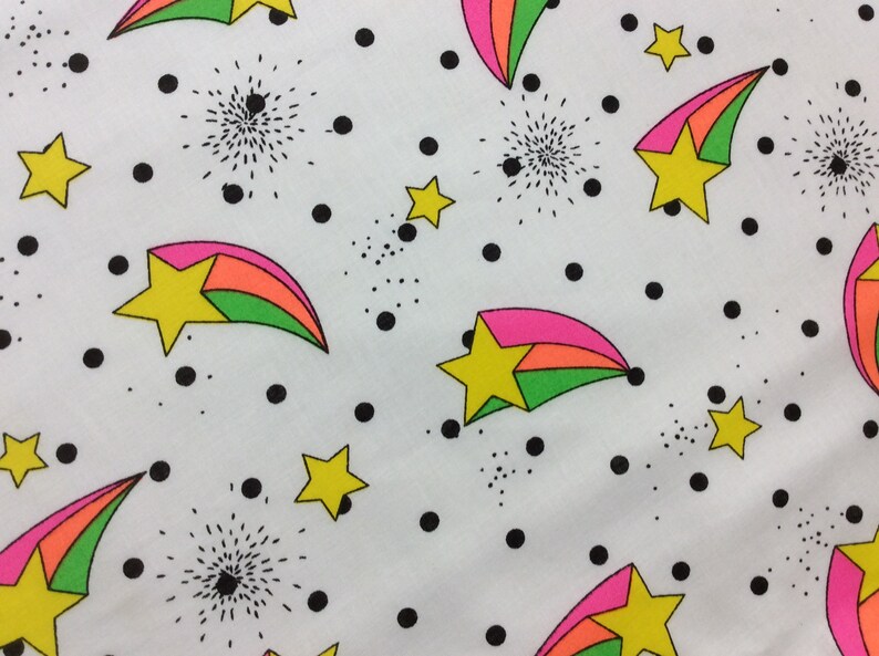 May include: White fabric with a repeating pattern of colorful shooting stars with pink, orange, and green stripes. The background is white with black polka dots.