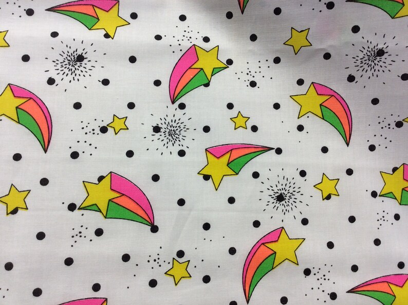 May include: White fabric with a repeating pattern of colorful shooting stars and black polka dots. The stars are yellow with pink, orange, and green stripes.