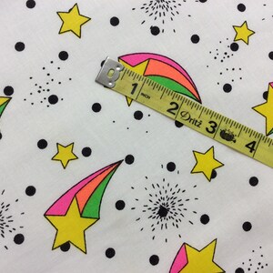 May include: White fabric with a repeating pattern of black dots, green, pink, and yellow shooting stars, and black firework designs. A yellow measuring tape with black markings reads "1 inch, 2 Dritz, 3, 4, 5".