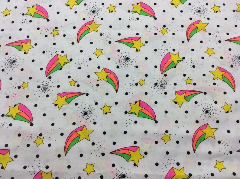 May include: White fabric with a repeating pattern of pink, green, and yellow shooting stars on a white background with black polka dots.