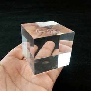 May include: A clear acrylic cube with the text "Doms Creations" printed on one side. The cube is being held in a person's hand.