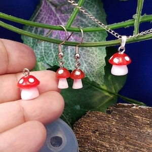 Peut inclure: Un ensemble de boucles d'oreilles et d'un collier en forme de champignon rouge et blanc. Les breloques en forme de champignon ont des points blancs et sont en pâte polymère. Les boucles d'oreilles sont argentées et ont une fermeture à crochet. Le collier est argenté et a un fermoir à mousqueton.