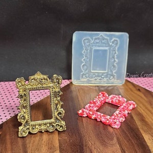 Könnte beinhalten: Ein verzierter Bilderrahmen in Goldfarbe mit einer durchsichtigen Plastikform desselben Rahmens. Ein pinkfarbener Glitzerbilderrahmen ist ebenfalls abgebildet.