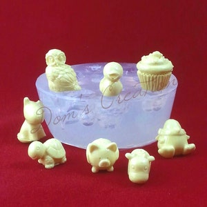 May include: A silicone mould with eight cavities for making small cake pops or other treats. The mould features a variety of designs, including an owl, a duck, a cupcake, a turtle, a pig, a cow, and two other animal designs.