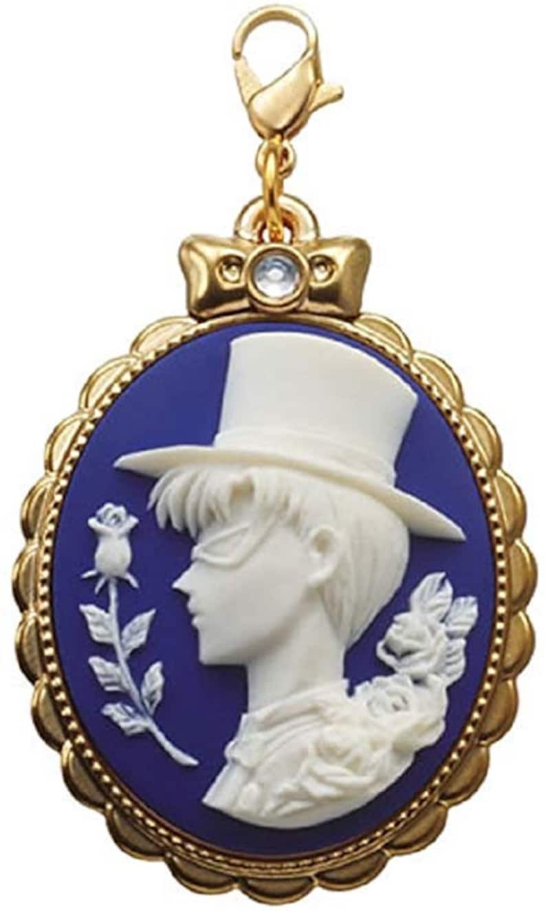 May include: A gold-tone charm featuring a cameo of a man in a top hat and a rose. The cameo is set in a blue enamel oval frame with a gold border.