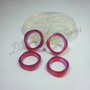 May include: Four pink and red resin rings, with a clear silicone mold in the background. The mold has four empty ring-shaped cavities.