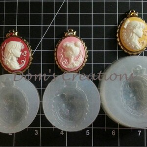 May include: Three silicone molds for making cameo pendants. The molds are round and feature a raised design of a woman's profile with a crown. The molds are shown next to three finished cameo pendants, one with a red background, one with a pink background, and one with a yellow background.
