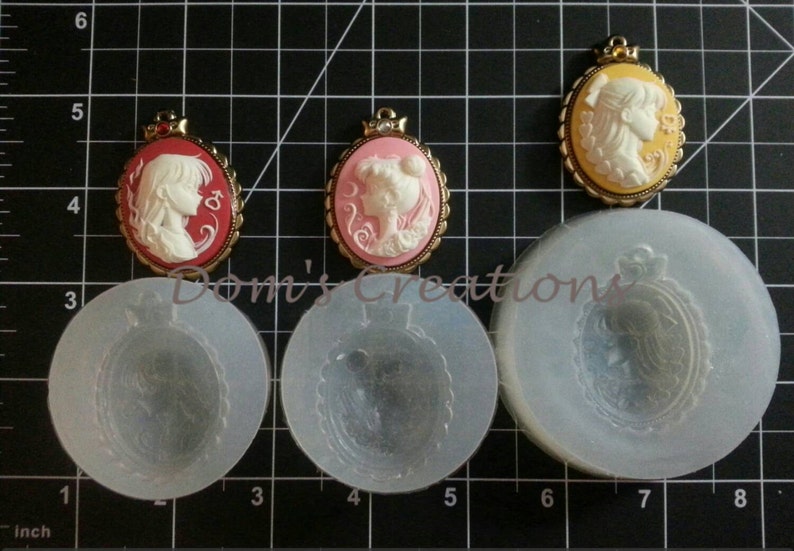 May include: Three silicone molds for making cameo pendants. The molds are round and feature a raised design of a woman's profile with a crown. The molds are shown next to three finished cameo pendants, one with a red background, one with a pink background, and one with a yellow background.