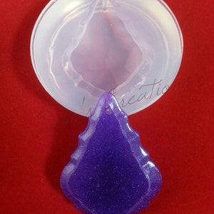 May include: A clear silicone mold for making a purple glitter resin pendant in the shape of a teardrop.