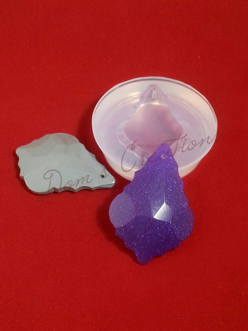 May include: A clear silicone mold for making a pendant in the shape of a pointed leaf. A purple leaf pendant with glitter is shown next to the mold.