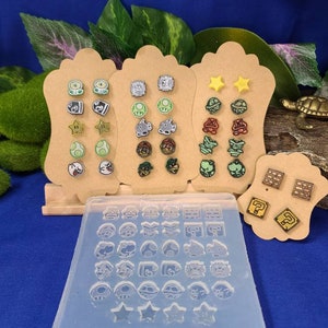Könnte beinhalten: Ein Set mit 36 Ohrringformen zum Thema Nintendo, mit Charakteren und Gegenständen aus der Super Mario Bros.-Reihe. Die Formen sind aus klarem Silikon und werden auf einem Holzbrett mit Beispielohrringen präsentiert.