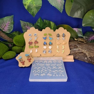 May include: A set of 24 resin molds for making nautical themed earrings. The molds are arranged on a clear plastic sheet with the text "Dome Creations" printed on it. The molds feature various designs including seashells, anchors, seahorses, and crabs.
