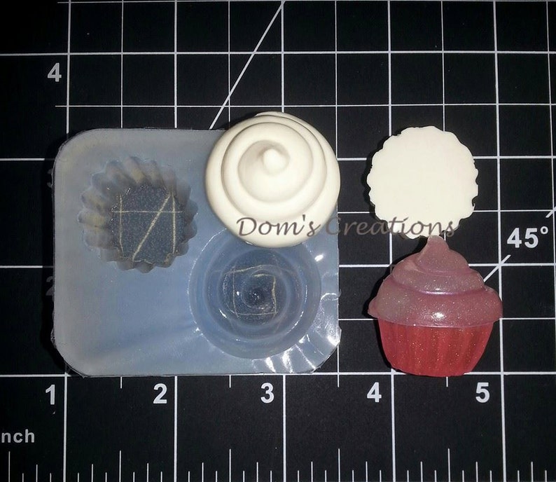May include: A silicone mold for making cupcake toppers. The mold has three cavities: one for a cupcake, one for a swirl, and one for a round topper. There is also a pink cupcake topper with glitter on top.