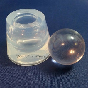 May include: A clear silicone mold for making a sphere, with a clear glass sphere sitting next to it. The mold is labeled "Dom's Creations".