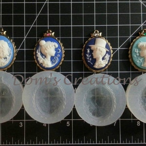 May include: Four cameo-style pendants with gold frames and blue, green, and white enamel. The pendants feature a white silhouette of a person's head and shoulders. The pendants are displayed on a white grid background with four clear silicone molds.