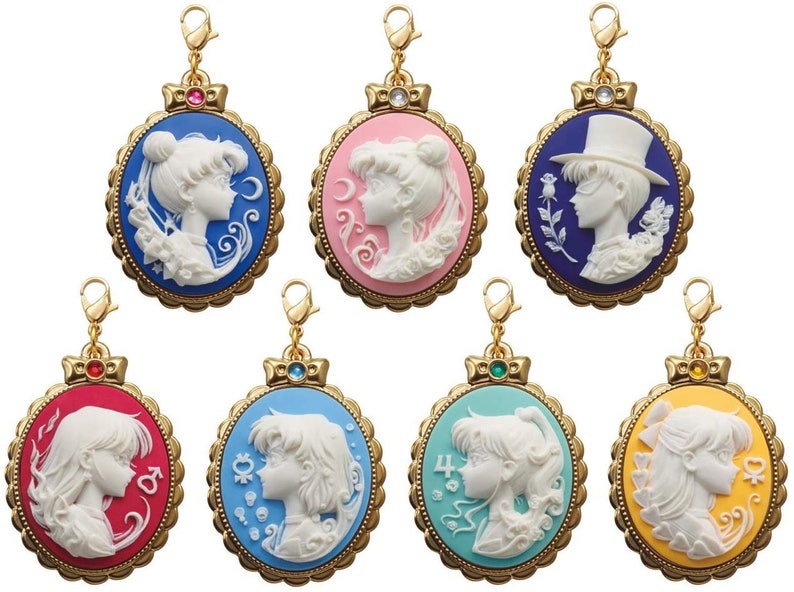 May include: Set of eight gold-tone charm pendants featuring cameo-style portraits of characters from the anime Sailor Moon. Each pendant has a different colored background and features a different character.