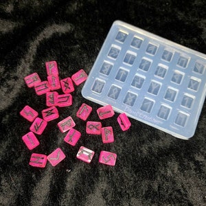 May include: A clear silicone mold with 25 square cavities, each containing a different rune symbol.  Pink resin casts of the runes are scattered around the mold.  The mold is labeled "Dims Creations".