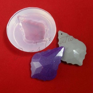 May include: A clear silicone mold for making resin jewelry. The mold is shaped like a leaf with a pointed tip. Two finished resin pieces are shown, one purple and one gray.