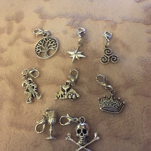 May include: A set of nine silver charm pendants with various designs, including a tree, a star, a spiral, a jester, a heart with a dog, a crown, a goblet, and a skull and crossbones.